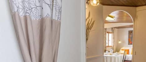 A hallway with a beige curtain, a wooden ceiling, and a dining area with a table and chairs.