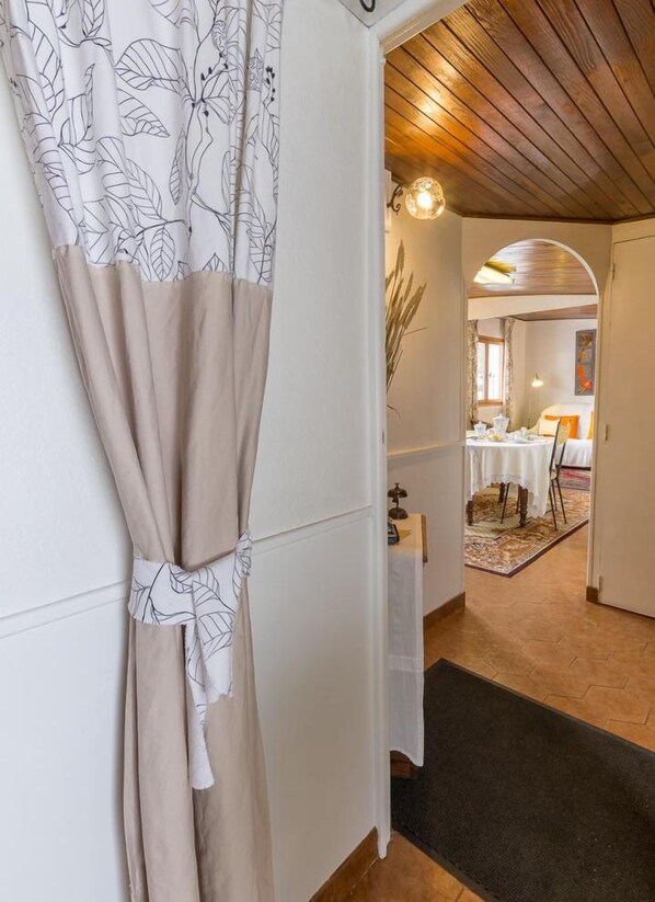 A hallway with a beige curtain, a wooden ceiling, and a dining area with a table and chairs.