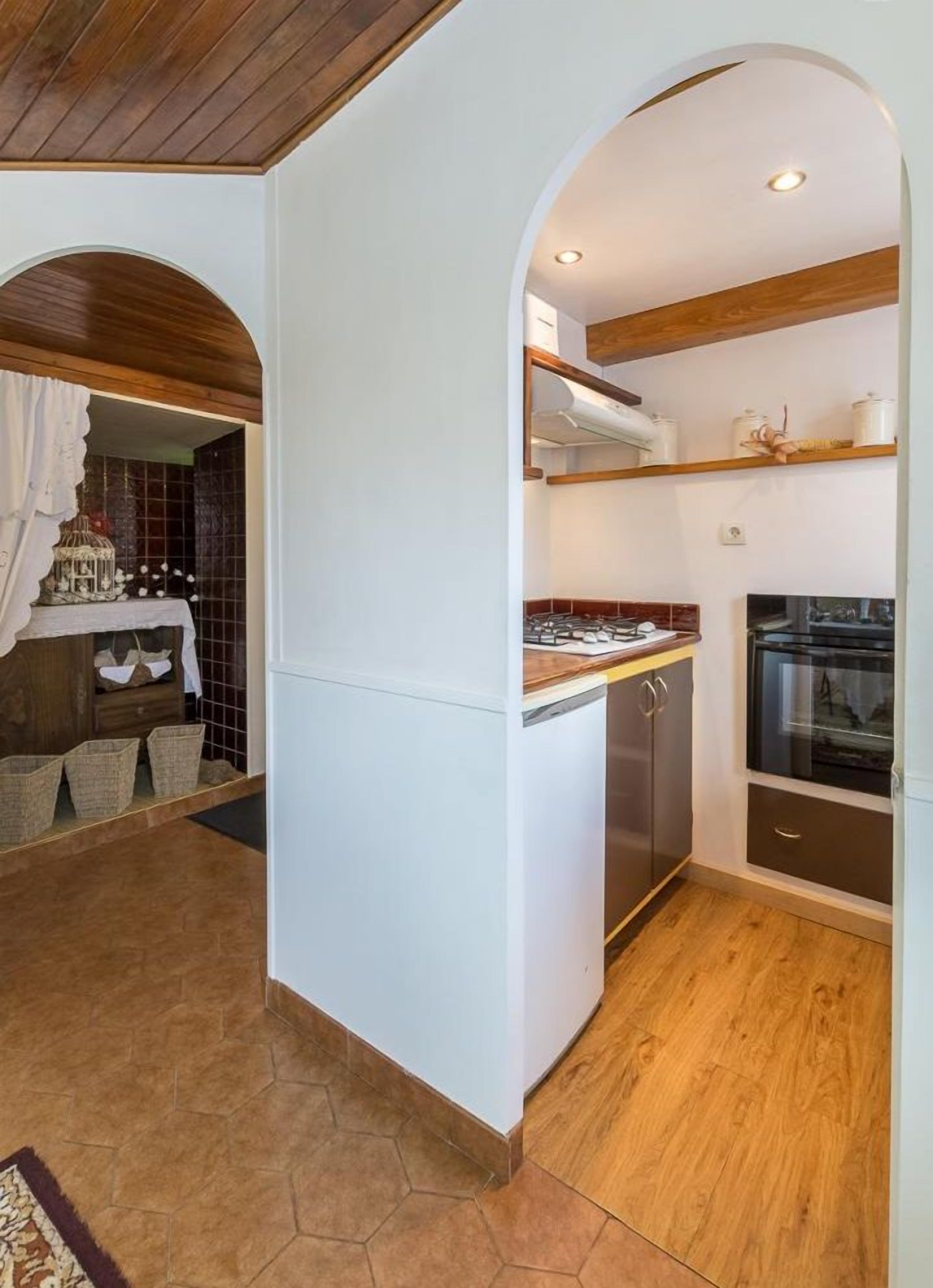 A compact kitchen with a gas stove, oven, and white cabinets. There is a wooden ceiling and a tiled floor.