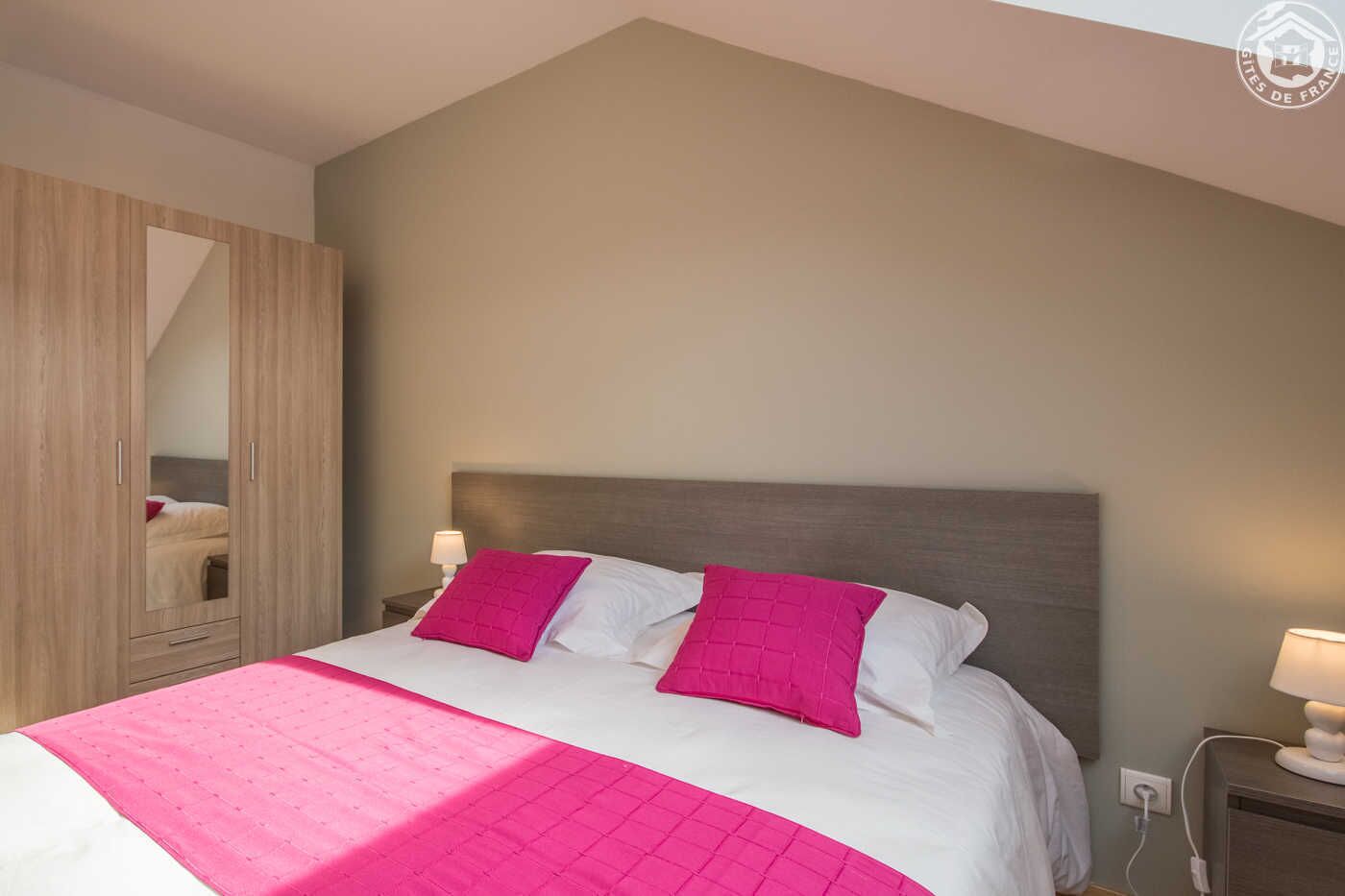 A bedroom with a bed, two bedside lamps, a nightstand, and a wardrobe.