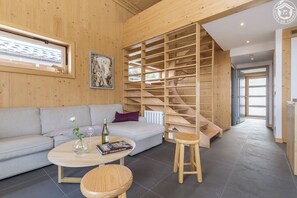 Ein modernes Interieur mit einer Holztreppe, einem grauen Sofa, einem runden Couchtisch und einem Bücherregal.