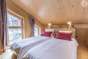 Ein Holzhüttenraum mit zwei Betten, einem Fenster und einer Deckenleuchte.