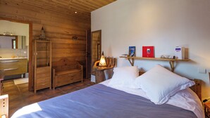 A wooden cabin-style bedroom with a bed, a wooden wardrobe, a mirror, and a shelf with books and a lamp.