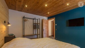 A bedroom with a bed, a wardrobe, a TV, and a wooden ceiling.