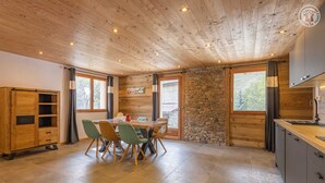 A spacious kitchen with a wooden ceiling, stone wall, and large windows.