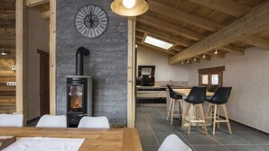 Un interior moderno con una pared de piedra, un reloj negro, un hogar de leña y una zona de comedor con taburetes de bar.