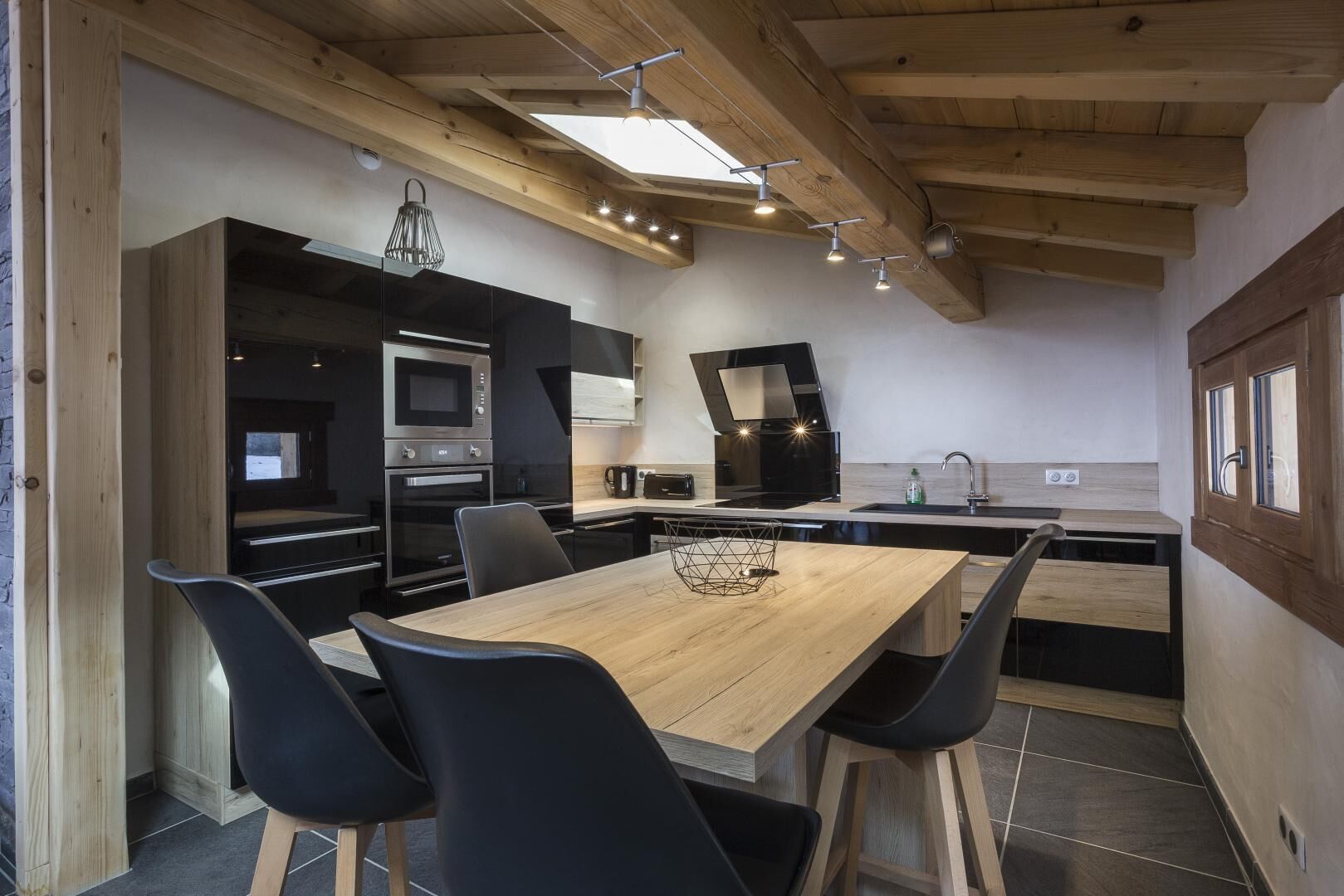 Eine moderne Küche mit einem Holzespeisetisch, schwarzen Stühlen, eingebauten Backöfen und einer schwarzen Arbeitsplatte.
