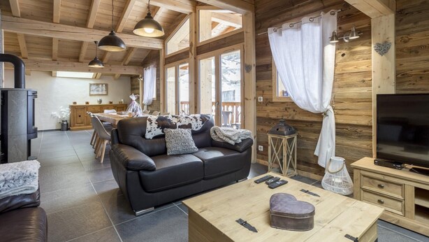 Interior acogedor de una cabaña con un sofá de cuero, una mesa de comedor de madera y un televisor.