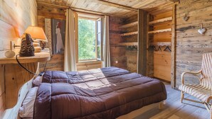 Een slaapkamer in een houten blokhut met een bed, een stoel, een lamp en een raam.