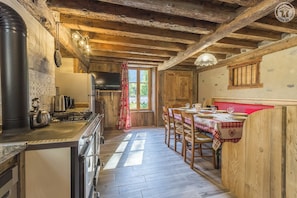 A rustic kitchen with a stove, kettle, and wooden beams.
