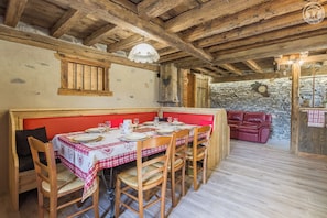 A rustic dining area with wooden furniture, a stone wall, and a red bench.
