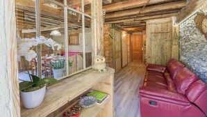 Een landelijk interieur met een houten plafond, een rode leren bank, een spiegel die een eethoek weerspiegelt, en een stenen muur.