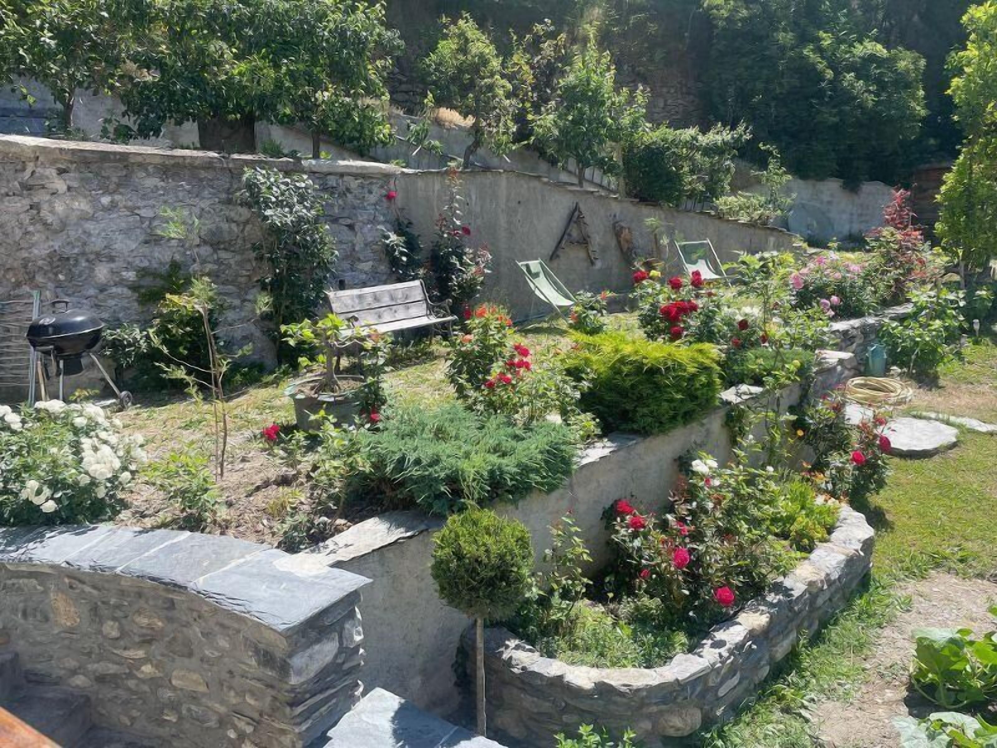 Un jardin avec des murs en pierre, un banc et un barbecue.