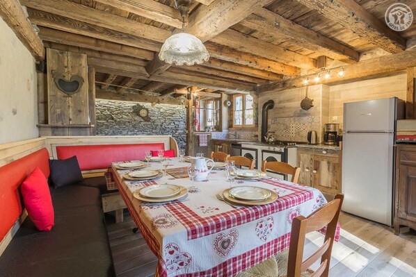 A rustic dining area with a wooden table set for four, a red bench, and a stone wall in the background.