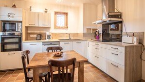 A modern kitchen with white cabinets, a wooden dining table, and a large window. - Chalet Belledonne - LA Thuile (LA THUILE)