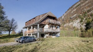 A two-story wooden chalet with balconies, a car parked in front, and a mountainous backdrop. - Chalet Belledonne - LA Thuile (LA THUILE)