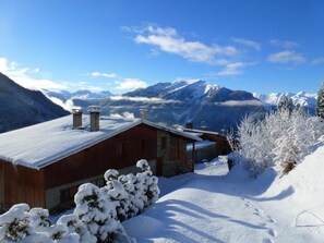 A wooden cabin with a snow-covered roof, a stone chimney, and a view of snow-capped mountains in the background. - LES Cabrettes - St-julien-montdenis (SAINT JULIEN MONTDENIS)