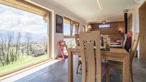Een moderne eetruimte met een houten tafel en stoelen, grote ramen met uitzicht op de omgeving, en een gezellig interieur met houten wanden en een kroonluchter.