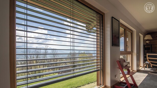 Een kamer met een groot raam, met uitzicht op een groen landschap en verre bergen.