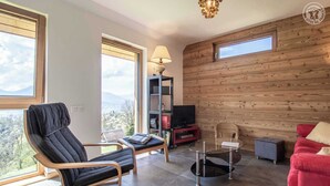 Een moderne woonkamer met een zwarte lounge fauteuil, een rode bank, een glazen salontafel en een houten wand.