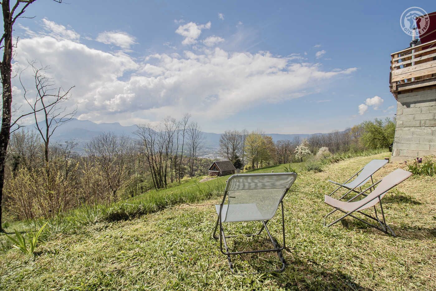 Un espace extérieur verdoyant avec deux chaises longues, un bâtiment en pierre et une vue sur des montagnes au loin.