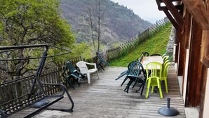 Una terraza de madera con mobiliario exterior, un sendero de piedra y vistas a un paisaje montañoso.