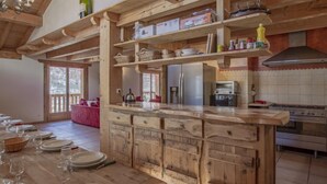 Una cocina rústica con armarios de madera, horno empotrado y comedor con un sofá rosa y mesa preparada para seis comensales.