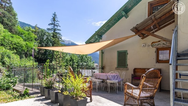Un patio con mobiliario exterior, plantas en macetas y una silla de madera.