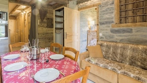 Un comedor rústico con una mesa de madera dispuesta para cuatro personas, una pared de piedra y un sofá cubierto de pieles.