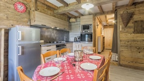 Una cocina rústica con vigas de madera, un refrigerador, estufa y una mesa de comedor preparada para cuatro.