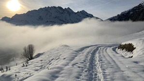Un sendero nevado en la montaña bajo un cielo despejado, con el sol poniéndose o saliendo.