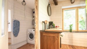 Una cucina compatta con mobili in legno, una lavatrice, una sveglia e una finestra con vista sul verde.