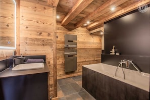 A modern bathroom with wooden walls, a large bathtub, a built-in sink, and a refrigerator. - LE Cocoon DES Neiges (LA FECLAZ LES DESERTS)