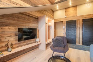 A modern interior with a wooden wall, a mounted TV, a seating area with a chair, and a small table with a decorative item. - LE Cocoon DES Neiges (LA FECLAZ LES DESERTS)