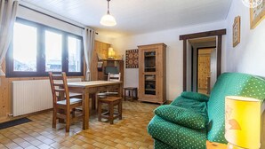 A cozy room with a wooden dining table, chairs, a green sofa, and a TV.