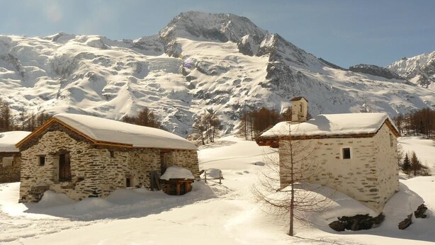 A snow-covered mountain village with stone buildings and a clear sky.