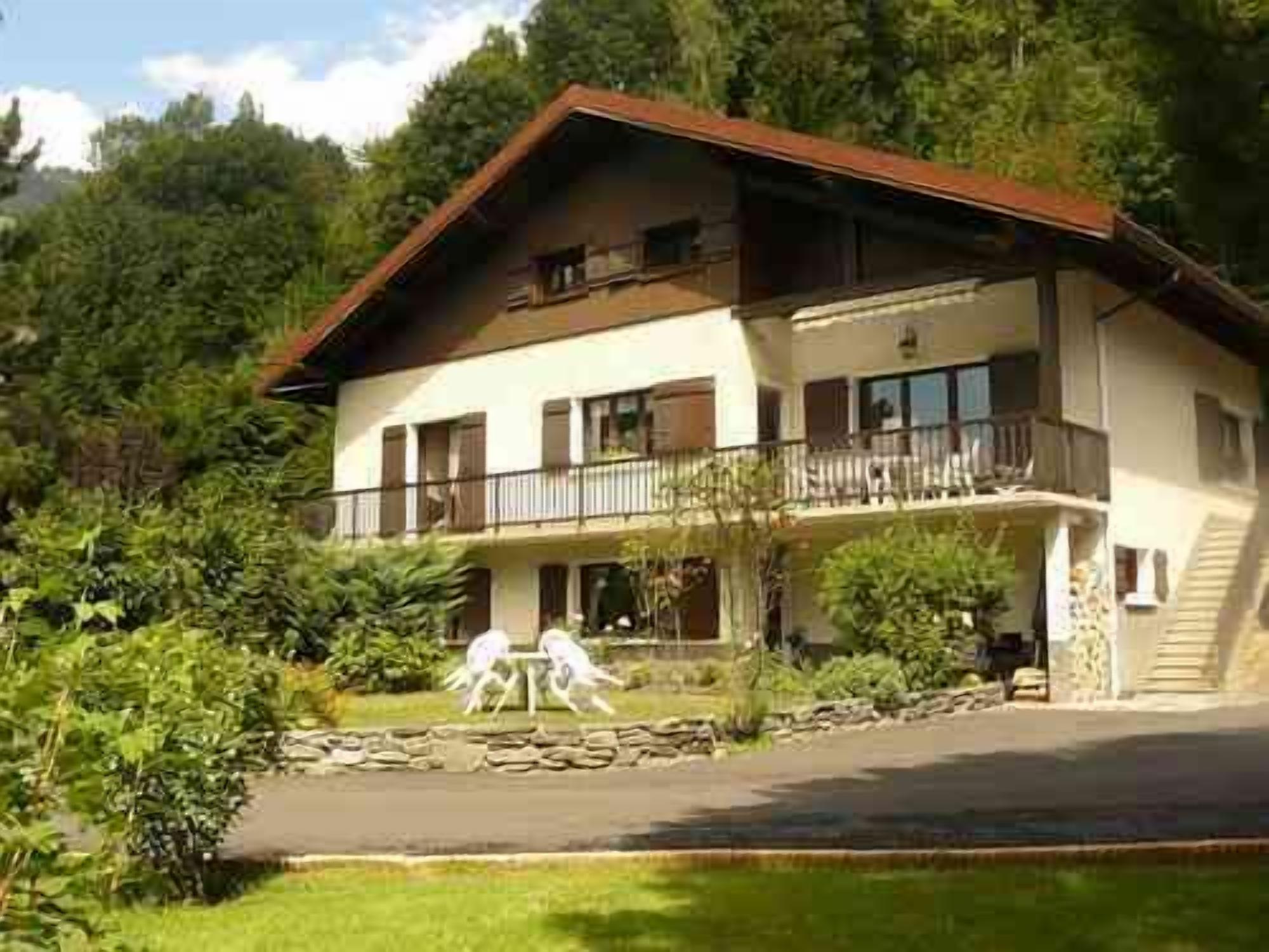 Una casa a due piani con un balcone, immersa nel verde e circondata da un muro in pietra.