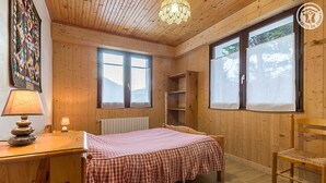 A wooden room with a bed, a chair, a desk, and a radiator.