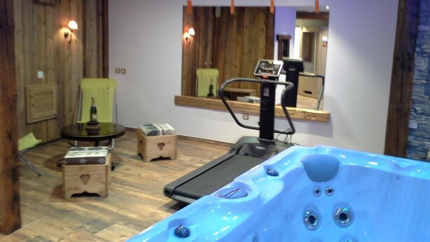 A room with a wooden floor, a treadmill, a massage chair, a small table with a bottle, and a wooden chest. - Chalet LES Ancolies - Valloire (VALLOIRE)
