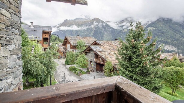 A mountain village with traditional wooden houses, stone walls, and a view of snow-capped mountains.