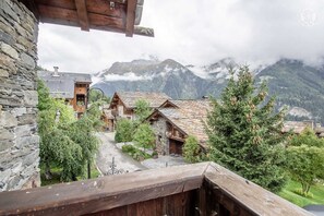 Een bergdorpsgezicht met traditionele houten huizen, stenen muren en een uitzicht op besneeuwde bergtoppen.