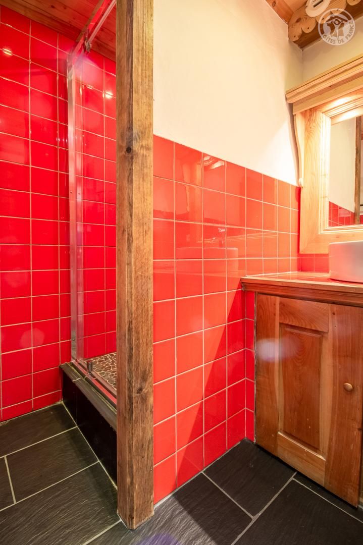 A bathroom with red tiles, a wooden column, a sink with a mirror, and a wooden cabinet.