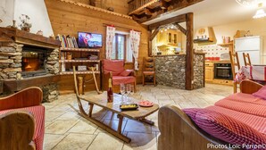 A cozy log cabin interior with a stone fireplace, wooden furniture, a television, and a kitchen area. - LE Glopet - Hauteluce-les-saisies (HAUTELUCE-LES-SAISIES)