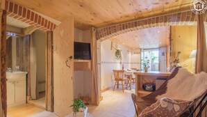 Ein gemütliches Interieur mit Holzbalkendecke, einem Essbereich mit Tisch und Stühlen, einer Couch und einem kleinen runden Tisch mit einer Pflanze.