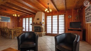 Ein gemütliches Holzhaus-Interieur mit Essbereich, zwei Ledersesseln, Kamin und Fernseher.
