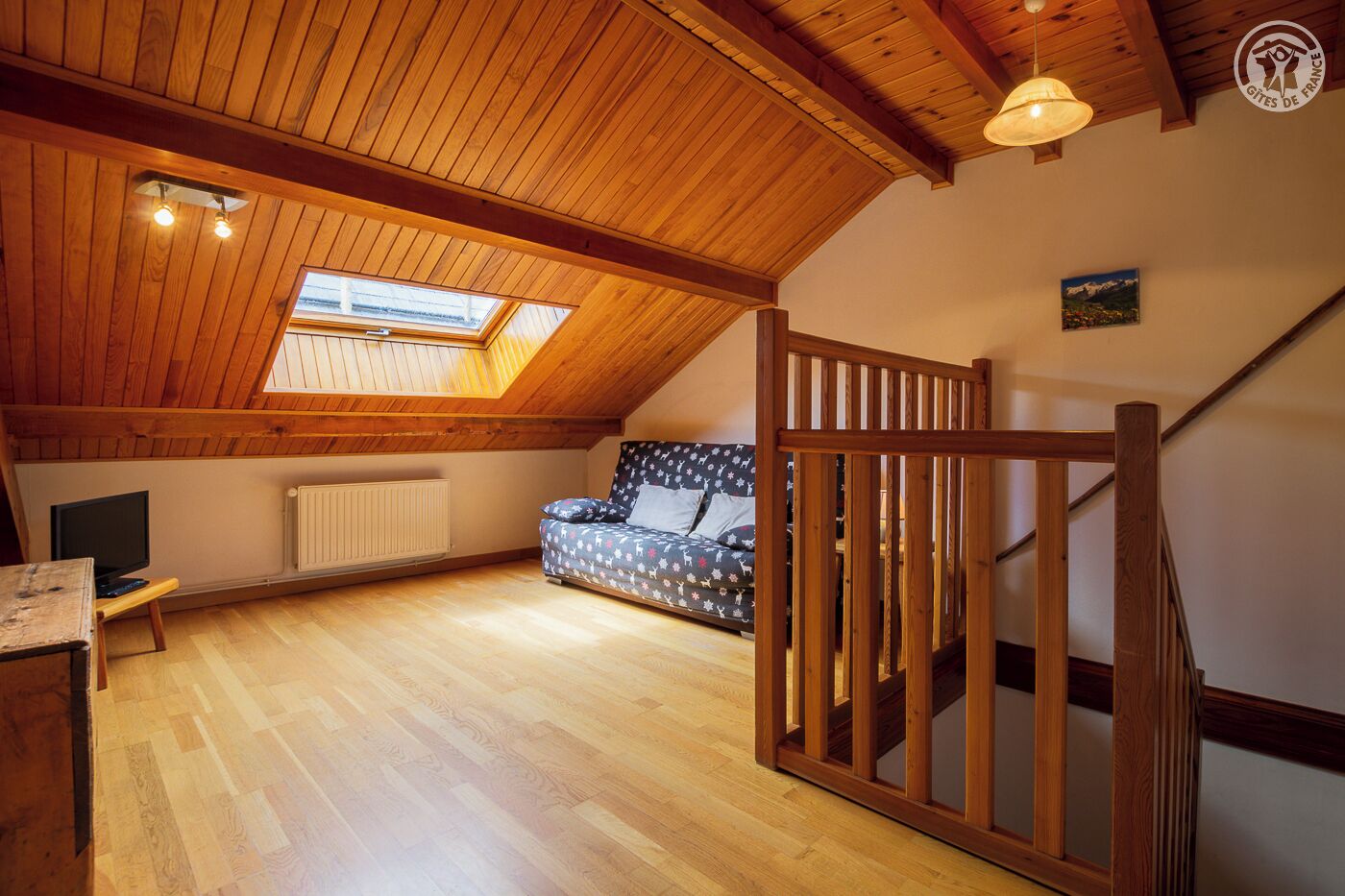 A cozy attic bedroom with a sloped ceiling, a skylight, a bed, a desk, and a chair.