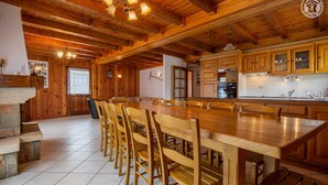 Ein geräumiger Essbereich mit Holzboden, einem langen Tisch und Stühlen, eine Küche mit Holzausstattung und ein Kamin aus Stein.