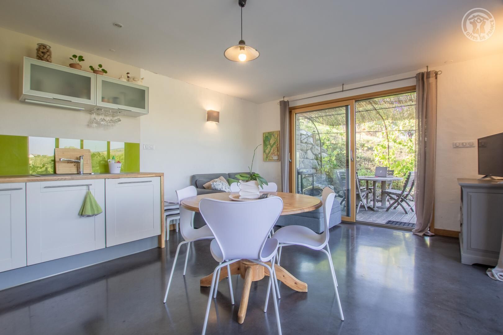 Una cocina moderna con armarios blancos, una mesa de comedor de madera y un amplio ventanal corredero que da a un patio exterior.