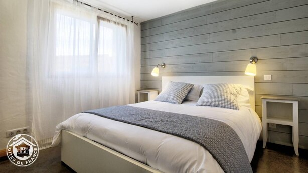 A bedroom with a large bed, two bedside tables, a window with sheer curtains, and a wooden wall panel. - L'aromatique - Chignin (CHIGNIN)