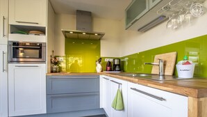 A modern kitchen with white cabinets, a stainless steel oven, a green backsplash, and a wooden countertop. - L'aromatique - Chignin (CHIGNIN)